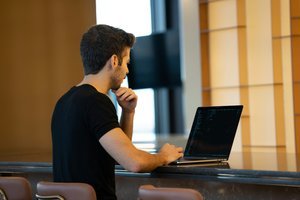 Un homme assis au bar, utilisant un ordinateur portable. Ambiance décontractée et moderne.