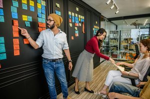 Une équipe de travail dans un bureau, avec des post-it colorés accrochés au mur.