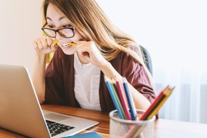 Une femme devant son ordinateur portable en train de mordre un crayon.